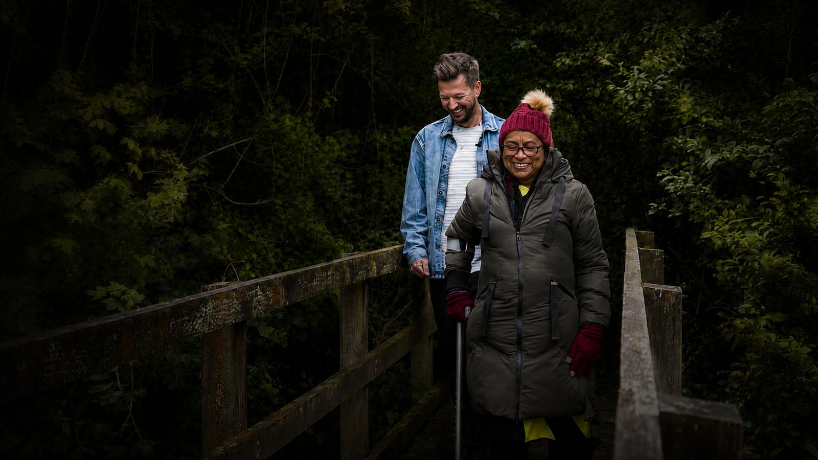 Josh Westover and a contributor stop on a wooden footbridge in a dark wood.